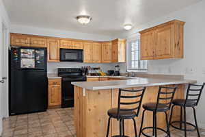 Kitchen with a breakfast bar, a peninsula, light countertops, black appliances, and a sink