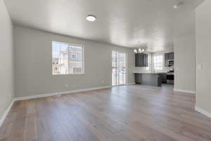 Unfurnished living room featuring light wood-style flooring, a textured ceiling, a sink, a notable chandelier, and baseboards