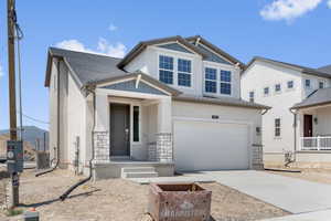 View of front of house with board and batten siding, a garage, stone siding, and concrete driveway