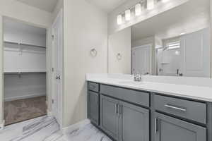 Full bath featuring baseboards, a spacious closet, vanity, marble finish floor, and a shower with shower door
