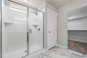 Full bath with a shower stall, marble finish floor, baseboards, and a spacious closet