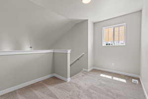Additional living space with carpet flooring, visible vents, baseboards, and lofted ceiling