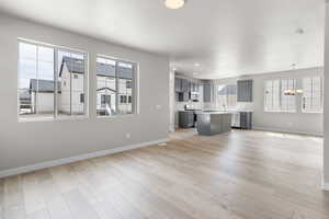 Unfurnished living room with light wood finished floors, a notable chandelier, and baseboards