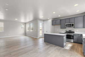 Kitchen featuring a kitchen island, gray cabinets, light countertops, stainless steel appliances, and light wood finished floors