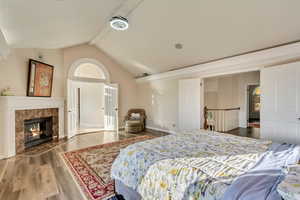 Bedroom with a fireplace, baseboards, wood finished floors, and lofted ceiling