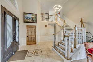 Entrance foyer with a towering ceiling, stairway, light tile patterned floors, a wainscoted wall, and a decorative wall