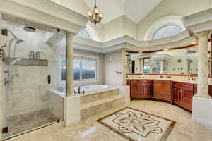 Bathroom featuring decorative columns, a bath, lofted ceiling, a stall shower, and double vanity