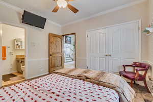 Carpeted bedroom featuring a closet, baseboards, ceiling fan, crown molding, and connected bathroom