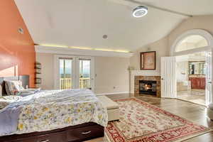 Bedroom with ensuite bathroom, access to outside, a fireplace, wood finished floors, and vaulted ceiling with beams