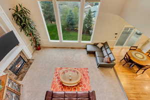 Carpeted living area with a fireplace with flush hearth, baseboards, lofted ceiling, and wood finished floors