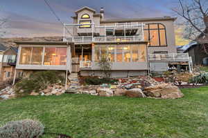 Rear view of house featuring a yard, a wooden deck, a sunroom, and a balcony