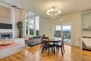 Dining room with plenty of natural light, light wood finished floors, a fireplace, and ceiling fan with notable chandelier