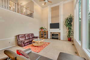 Carpeted living area with visible vents, baseboards, ornamental molding, ceiling fan, and a towering ceiling