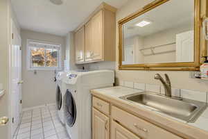 Laundry room featuring baseboards, washing machine and dryer, light tile patterned flooring, cabinet space, and a sink