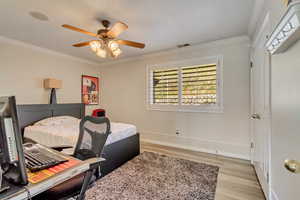 Bedroom featuring light wood finished floors, visible vents, baseboards, and ornamental molding