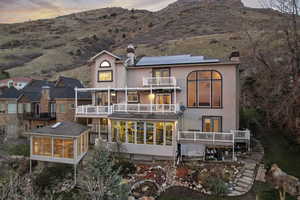 Back of house at dusk with a sunroom, a balcony, a chimney, and solar panels