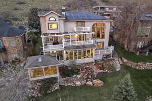 Back of house with a chimney, stucco siding, solar panels, and a balcony