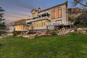 Back of property at dusk with a lawn, a balcony, a sunroom, and stucco siding