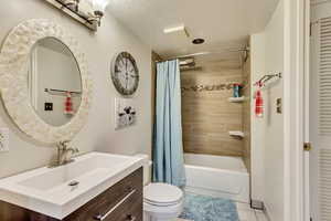 Bathroom featuring vanity, tile patterned flooring, a textured ceiling, toilet, and shower / bath combo with shower curtain