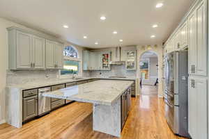 Kitchen with wall chimney exhaust hood, light wood-style flooring, arched walkways, a kitchen island, and stainless steel appliances