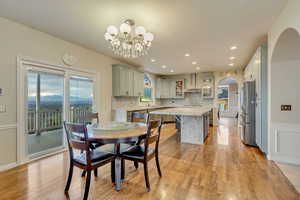 Dining room with arched walkways, light wood finished floors, a notable chandelier, and recessed lighting