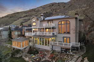 Back of house featuring a sunroom, a chimney, solar panels, and a balcony