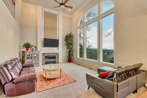 Living room with carpet, a ceiling fan, ornamental molding, a high ceiling, and a premium fireplace