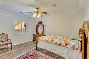 Bedroom with a tray ceiling, visible vents, light wood-type flooring, and baseboards