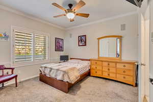 Carpeted bedroom featuring visible vents, baseboards, crown molding, and a ceiling fan