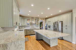 Kitchen featuring a kitchen island, wall chimney exhaust hood, stainless steel appliances, arched walkways, and a sink