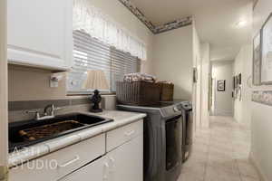 Clothes washing area featuring light tile patterned flooring, a sink, baseboards, cabinet space, and washer and clothes dryer