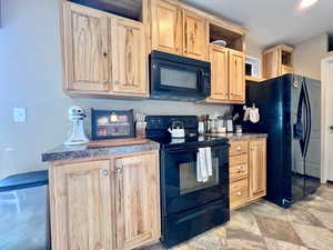 Kitchen with open shelves, black appliances, stone finish floor, and light brown cabinetry