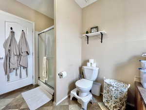 Full bath featuring toilet, a stall shower, stone finish floor, and baseboards