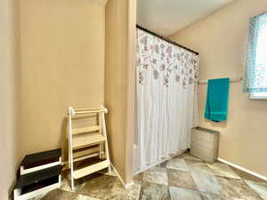 Full bath featuring stone finish flooring, shower / bath combination with curtain, and baseboards