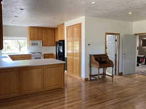 Kitchen with a textured ceiling, a peninsula, light countertops, white appliances, and light wood-style flooring