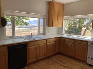 Kitchen with black dishwasher, light countertops, light wood-style floors, brown cabinets, and white range with electric cooktop