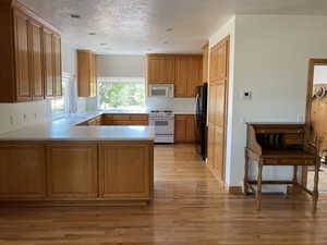 Kitchen with a peninsula, light wood-type flooring, white appliances, light countertops, and a textured ceiling