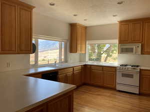 Kitchen featuring white appliances, light countertops, a textured ceiling, brown cabinets, and light wood-style flooring