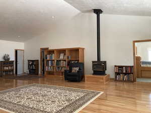 Sitting room featuring a wood stove, a textured ceiling, light wood-style floors, and high vaulted ceiling
