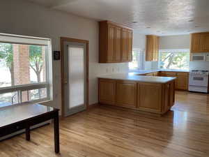 Kitchen featuring white appliances, light wood-type flooring, light countertops, and a peninsula