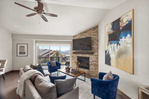 Living room with baseboards, lofted ceiling, a ceiling fan, wood finished floors, and a stone fireplace