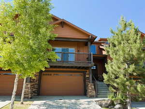 View of front of house with a balcony, a garage, driveway, board and batten siding, and stone siding