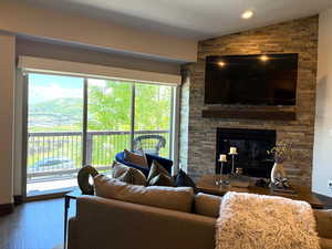 Living room featuring vaulted ceiling, a stone fireplace, and wood finished floors