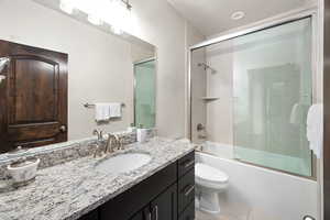 Full bath with combined bath / shower with glass door, vanity, tile patterned floors, and toilet