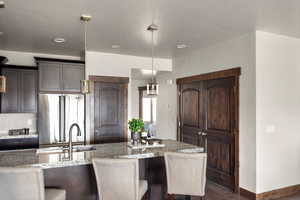 Kitchen featuring high quality fridge, a sink, decorative backsplash, light stone countertops, and hanging light fixtures