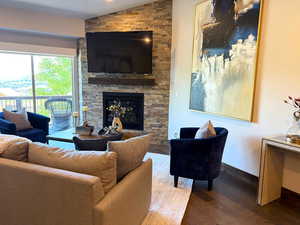 Living room featuring dark wood finished floors, lofted ceiling, and a stone fireplace