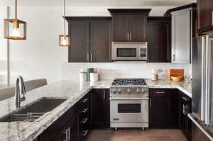 Kitchen featuring light stone counters, premium appliances, a sink, dark brown cabinetry, and backsplash