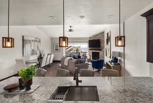 Kitchen featuring lofted ceiling, a ceiling fan, a sink, light stone countertops, and a fireplace