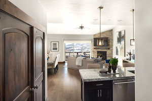 Kitchen with dark wood-style floors, stone countertops, decorative light fixtures, a fireplace, and ceiling fan