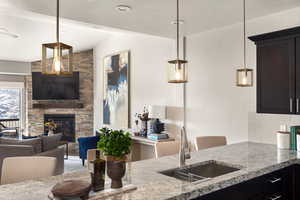 Kitchen with a sink, open floor plan, lofted ceiling, light stone counters, and a stone fireplace